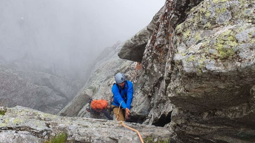 An einer steilen Felswand mit grauem Gestein klettert Bergführer Klaus Petz in blauer Jacke und weißem Helm.