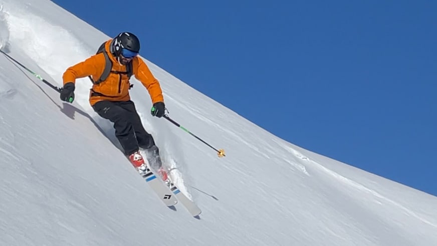 Bergführer Klaus Petz fährt in orangefarbener Winterjacke einen steilen Schneehang mit unverspurtem Pulverschnee hinab.