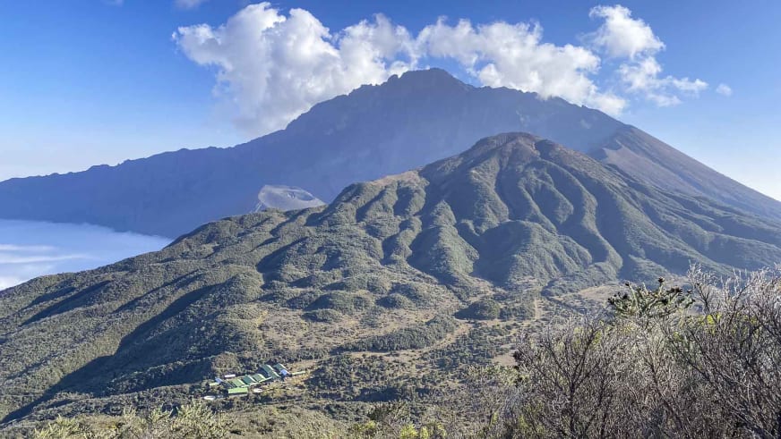 Panorama des Mount Meru Vulkankegels mit der Sattelhütte (Mt. Meru) als helle Gebäude im Mittelgrund.