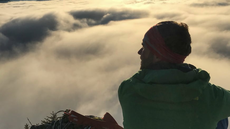 Bergwanderführer Benjamin Mäder mit Sonnenbrille und grüner Jacke blickt über eine ausgedehnte Wolkendecke.