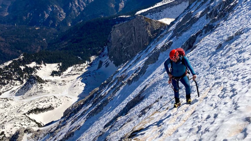 Bergwanderführer Dennis Brida steigt mit Eispickel einen steilen schneebedeckten Hang in hochalpiner Berglandschaft auf.