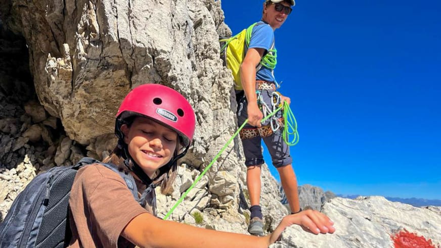 Zwei Personen beim Klettern an heller Kalksteinwand, Bergführer Silvestro Franchini im Hintergrund mit Kletterausrüstung am Gurt.