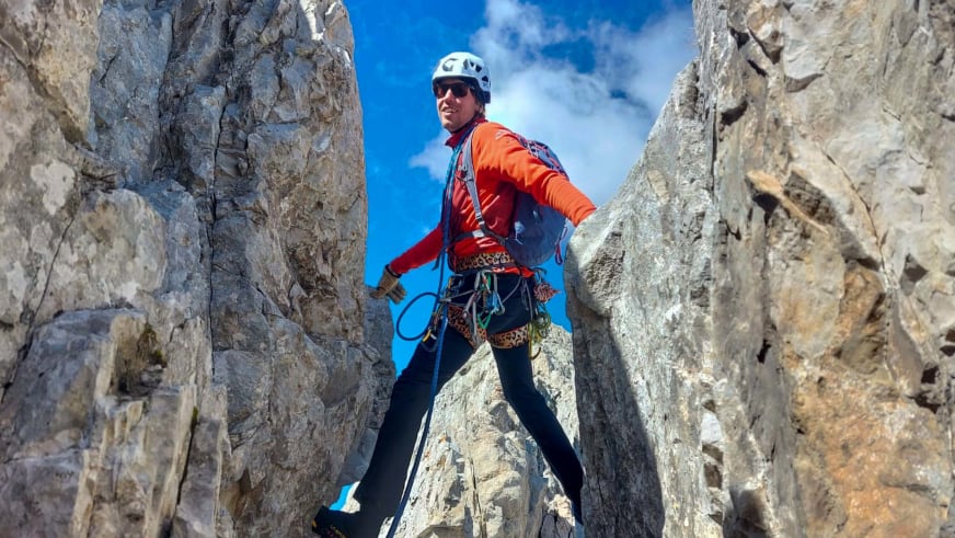 In kaminartiger Felsspalte zwischen Kalksteinwänden steht Bergführer Silvestro Franchini mit weißem Helm und Klettergurt.