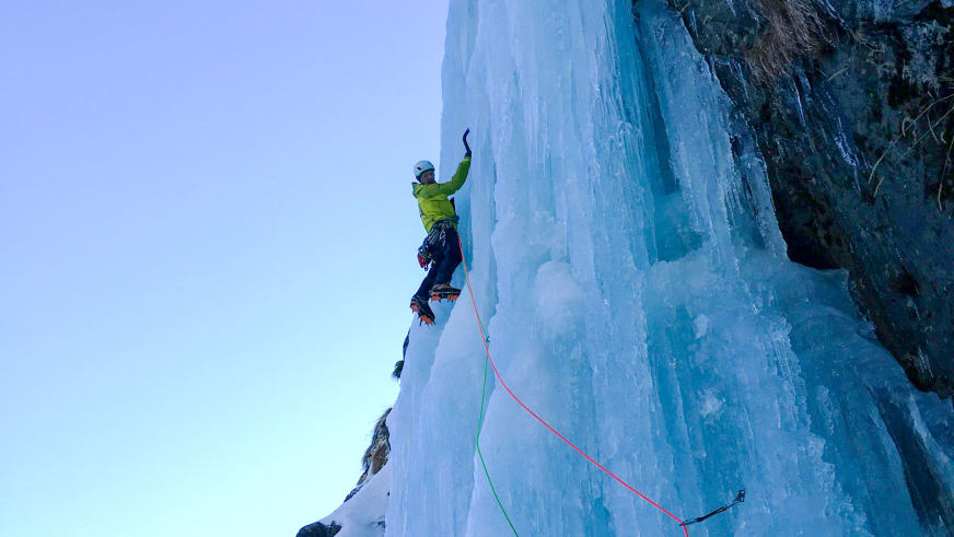 Bergführer Klaus Karlstätter klettert in gelber Jacke mit Eispickel und Steigeisen an einer blauen Eiswand, gesichert am rot-grünen Seil.