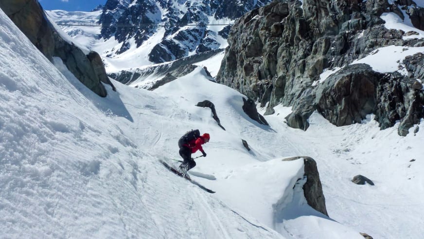 Bergführer Klaus Karlstätter fährt in roter Jacke auf Skiern einen verschneiten Hang hinab, im Hintergrund alpine Felswände.