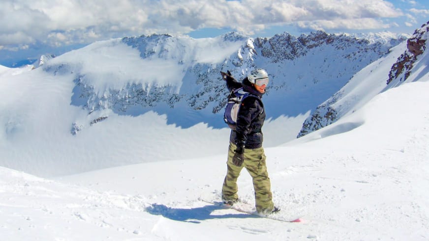 Im verschneiten Hochgebirge steht Bergführer Markus Arzberger auf einem Snowboard und blickt zu den schneebedeckten Gipfeln.