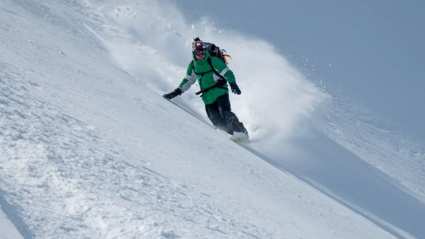 Bergführer Markus Arzberger fährt in grüner Winterjacke auf seinem Snowboard durch unverspurten Pulverschnee einen steilen Hang hinab.