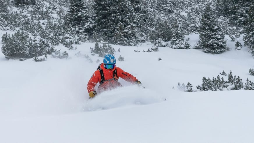 Bergführer Alessandro Lucchi in roter Jacke und blauem Helm wirbelt bei der Abfahrt durch Pulverschnee eine große Schneewolke auf.