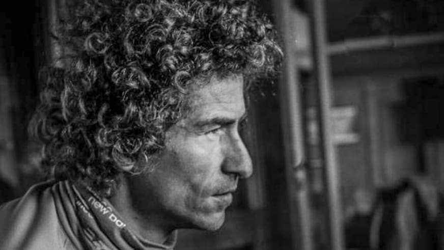 Schwarz-weiß Portrait zeigt Bergführer Alessandro Lucchi mit lockigem Haar im Profil, er trägt Outdoor-Bekleidung in Innenraum.