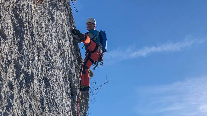 Mit roter Hose und weißem Helm klettert Bergwanderführer Horst Kopelent an einer senkrechten grauen Felswand mit Klettergurt.