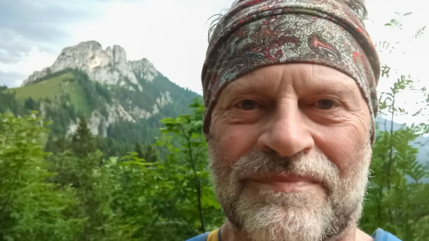 Bergwanderführer Horst Kopelent mit grauem Vollbart und gemusterter Kopfbedeckung vor alpiner Landschaft mit Kalksteinfels.