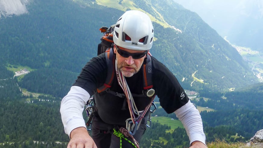 Mit weißem Helm und schwarzem Klettergurt steht Bergwanderführer Horst Kopelent am Fels über einem grünen Alpental.
