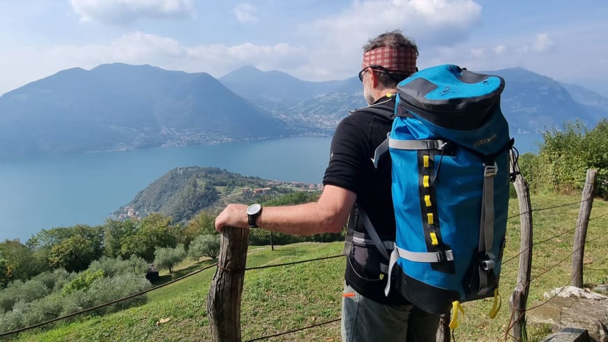 Bergwanderführer Horst Kopelent mit rot-weiß kariertem Stirnband und blauem Rucksack blickt über einen großen Alpensee.