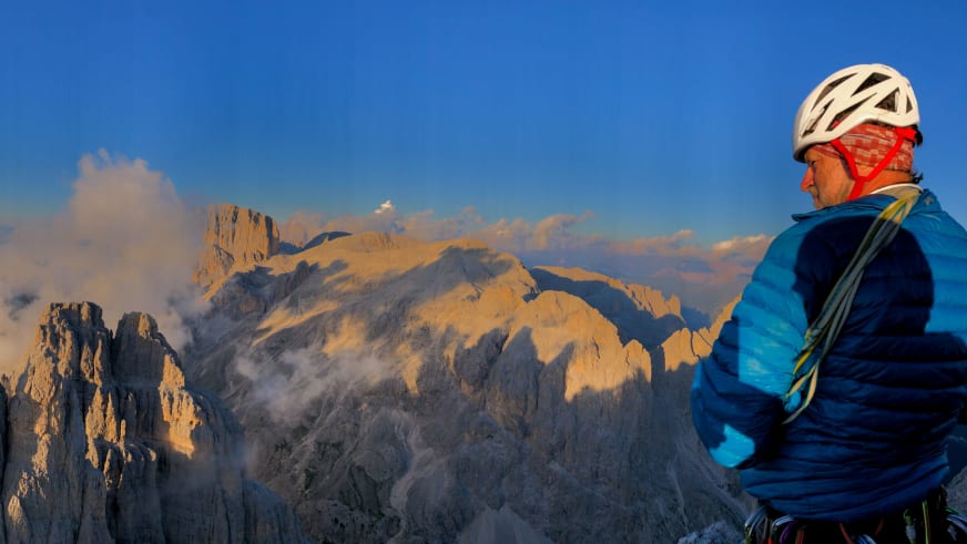 Bergwanderführer Horst Kopelent mit weißem Helm und rotem Tuch blickt zu den Dolomiten-Felswänden bei goldener Abendsonne.