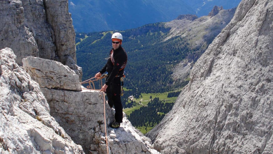 Auf schmalem Felsvorsprung aus Kalkstein steht Bergwanderführer Horst Kopelent mit orangenem Seil und weißem Helm.