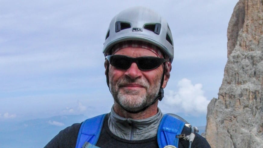 Bergwanderführer Horst Kopelent trägt weißen Petzl-Helm und blauen Klettergurt vor heller Felswand und blauem Himmel.