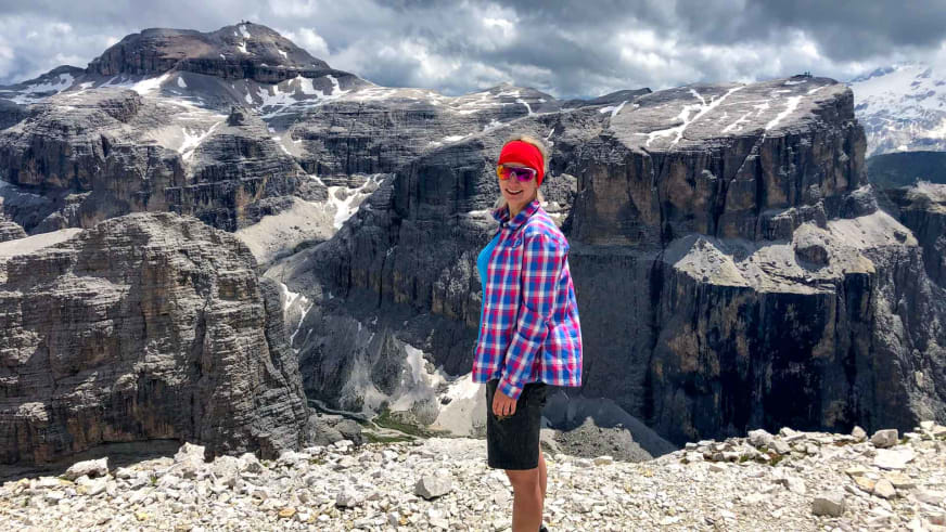 Bergwanderführerin Stefanie Erdmann steht lächelnd auf einem Geröllfeld vor der Dolomitenkulisse mit roter Mütze und kariertem Hemd.