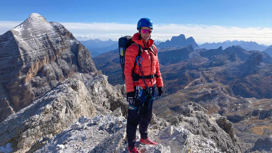 Bergwanderführerin Stefanie Erdmann steht mit blauem Helm und Klettersteig-Set auf Dolomitengipfel.