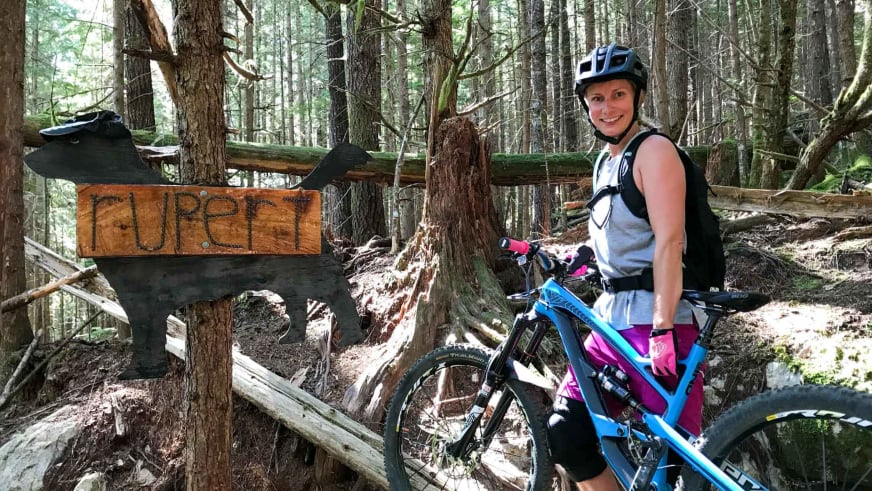 Mit blau-weißem Helm steht Bergwanderführerin Stefanie Erdmann neben blauem Mountainbike im Nadelwald.
