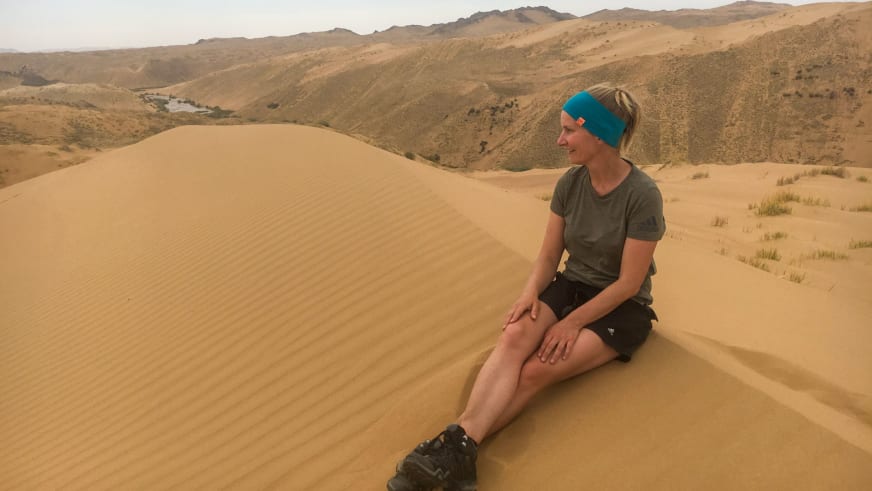 Auf sandigem Dünenkamm in Wüstenlandschaft sitzt Bergwanderführerin Stefanie Erdmann in olivgrünem Shirt.