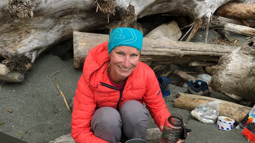 Zwischen angeschwemmten Baumstämmen sitzt Bergwanderführerin Stefanie Erdmann mit Thermosflasche am Strand.
