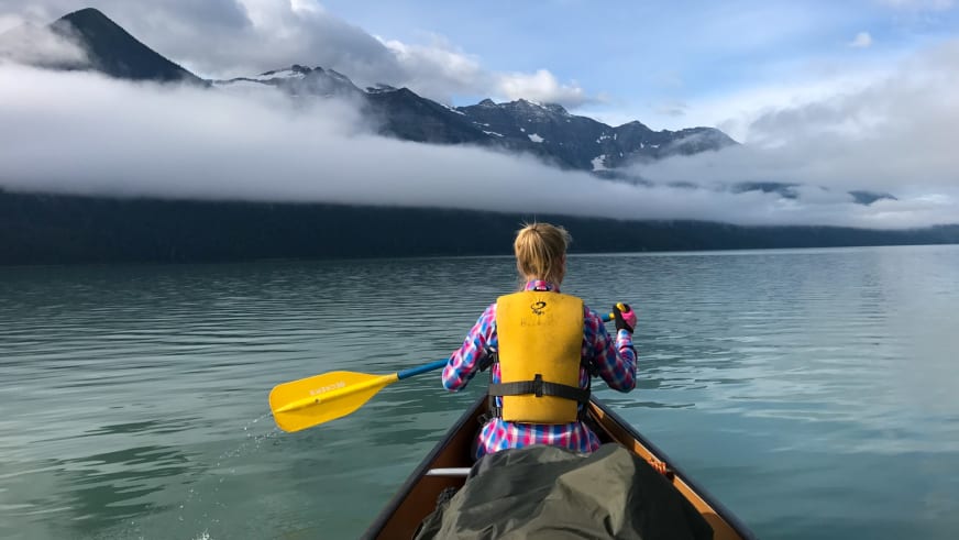 Bergwanderführerin Stefanie Erdmann paddelt in gelbem Schwimmweste in Holzkanu auf ruhigem See.