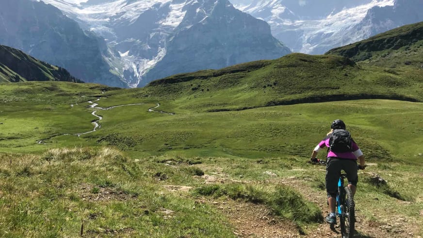 Auf türkisem Mountainbike fährt Bergwanderführerin Stefanie Erdmann über Erdweg durch Almwiesen.
