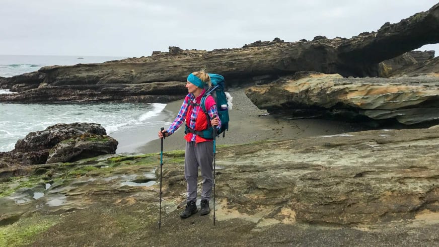 Bergwanderführerin Stefanie Erdmann steht mit türkisem Rucksack auf Felsplattform an geschichteter Küste.