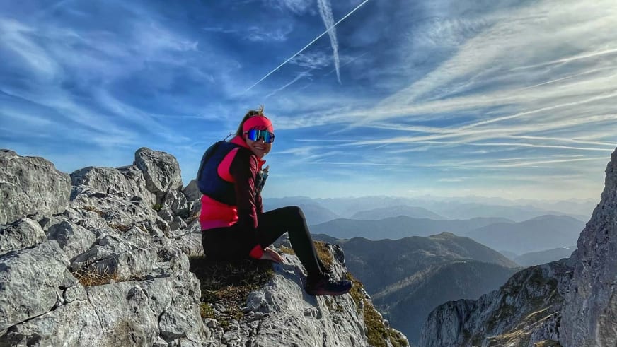 Bergwanderführerin Alina Elisabeth Leitinger sitzt auf einem Felsvorsprung in pinker Winterjacke und pausiert.