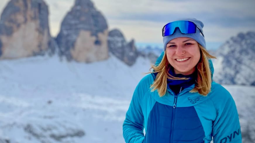 Lächelnd steht Bergwanderführerin Alina Elisabeth Leitinger in türkiser Winterjacke vor verschneiter Bergkulisse.