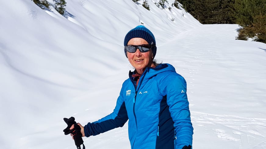 Bergwanderführerin Julia Riedl trägt blaue Winterjacke und Sonnenbrille vor verschneiter Berglandschaft im Winter.