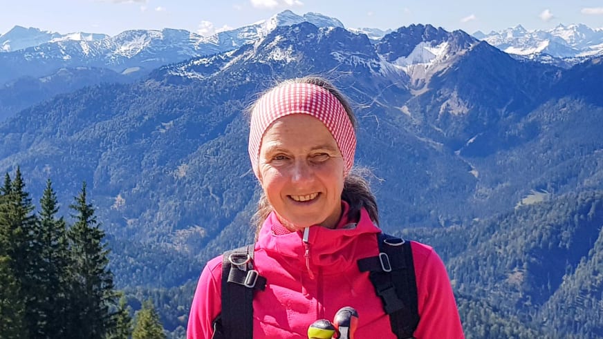 Portrait von Bergwanderführerin Julia Riedl mit rot-weiß kariertem Stirnband und pinker Softshelljacke vor Berglandschaft.