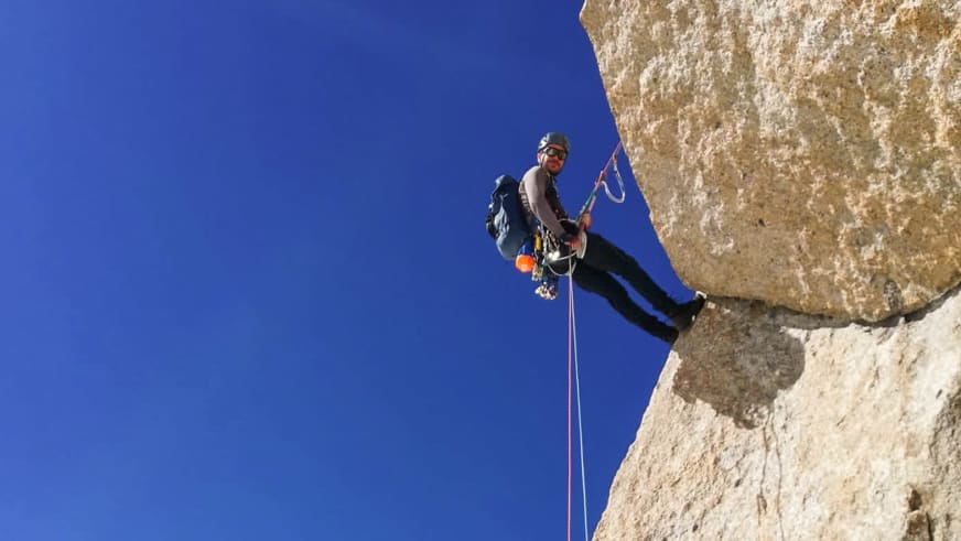 Mit Helm und Klettergurt hängt Bergführer Lukas Höllrigl am roten Seil an einer senkrechten Kalksteinwand.