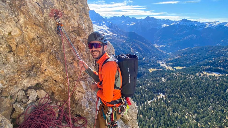 Bergführer Lukas Höllrigl in orangener Jacke hält Kletterseile und blickt vom Kalkfels ins Alpental hinab.