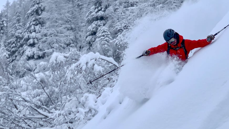 Durch tiefen Pulverschnee fährt Bergführer Lukas Höllrigl in roter Jacke zwischen schneebedeckten Nadelbäumen.