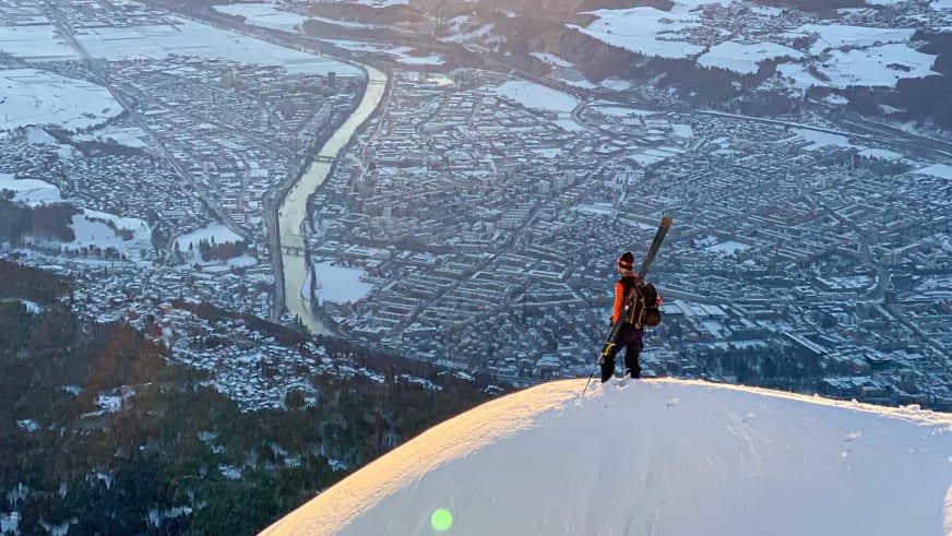 Bergführer Lukas Höllrigl steht auf verschneitem Hang und blickt auf die ausgedehnte Stadtlandschaft im Tal hinab.