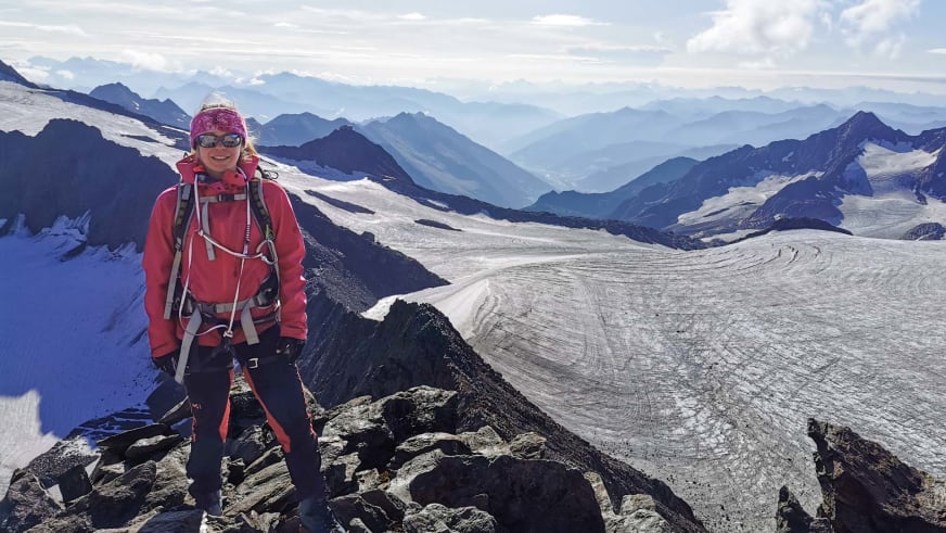 Auf einem Felsgrat steht Bergwanderführerin Patricia Neumair lächelnd vor einer weiten Gletscherlandschaft mit Spalten.