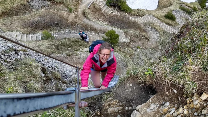 Bergwanderführerin Patricia Neumair klettert lächelnd an einer Stahlleiter eines Klettersteigs mit Drahtseil.
