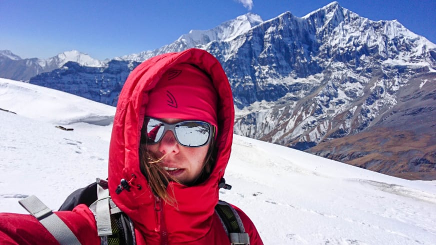 Bergwanderführerin Patricia Neumair trägt roten Daunenparka mit Kapuze und Gletscherbrille vor schneebedeckten Gipfeln.