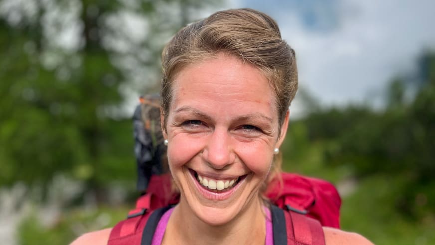 Bergwanderführerin Patricia Neumair lächelt breit in die Kamera und trägt rotes Funktionsshirt mit rotem Rucksack.