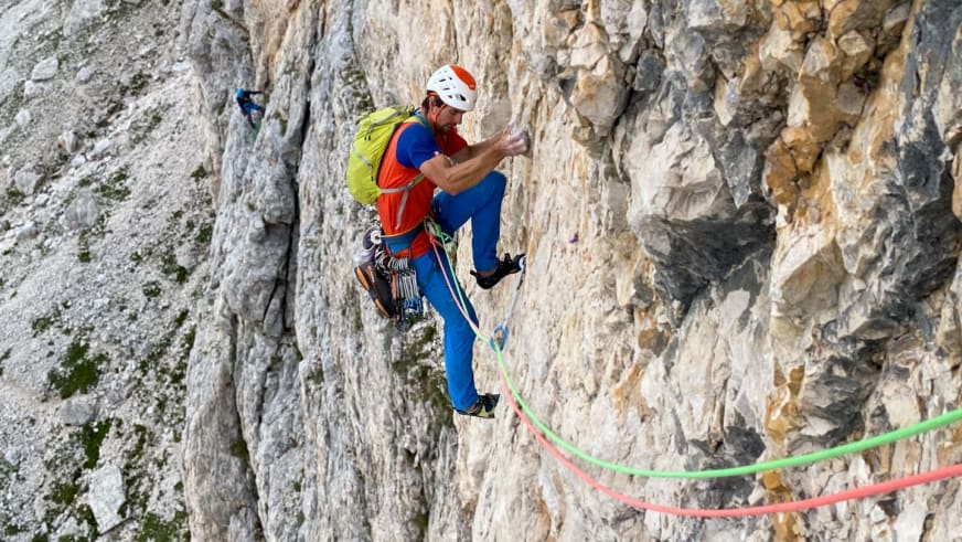 Bergführer Lukas Seedoch klettert frei an einer senkrechten Kalksteinwand mit grünem und rotem Kletterseil.