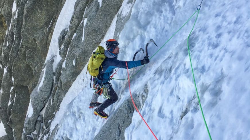 Bergführer Lukas Seedoch klettert mit zwei Eisgeräten an einer strukturierten Eiswand, gesichert über grünes Kletterseil.