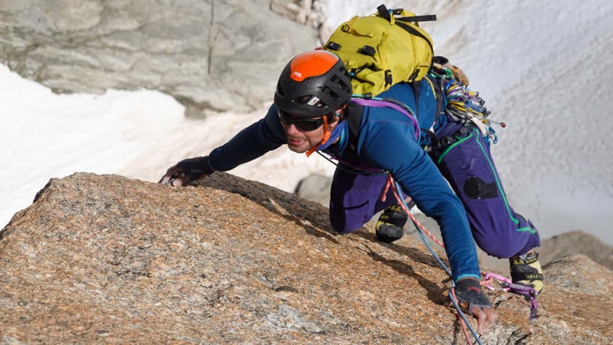 Bergführer Lukas Seedoch klettert aktiv an rötlich-brauner Granitwand in Chamonix mit gelbem Rucksack.