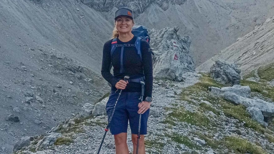In blauer Wanderausrüstung hält Bergwanderführerin Madlen Bucher zwei Wanderstöcke in hochalpinem Kalksteingelände.