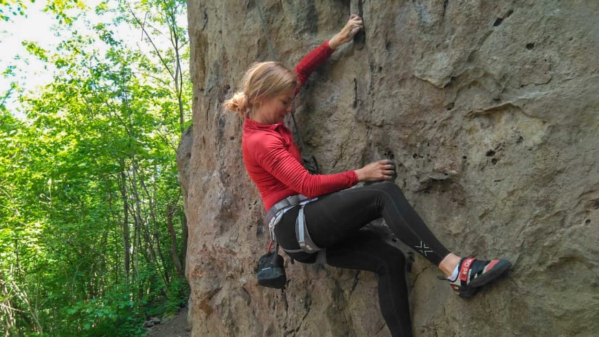 Bergwanderführerin Madlen Bucher klettert in rotem Shirt mit Klettergurt und roten Kletterschuhen an heller Felswand.