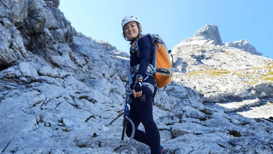 Mit weißem Kletterhelm und Klettersteig-Set steht Bergwanderführerin Madlen Bucher lächelnd auf hellem Kalksteinfels.