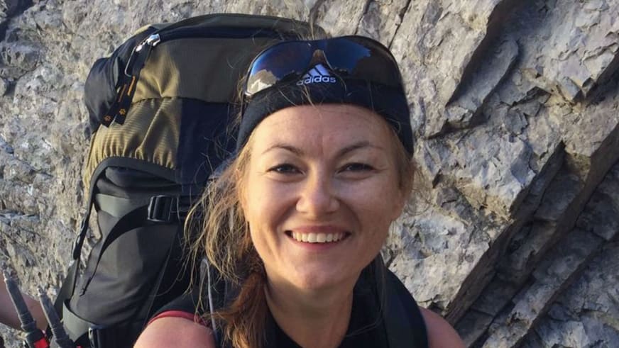 Portrait von Bergwanderführerin Madlen Bucher mit blauer Adidas-Kappe und großem schwarzen Trekkingrucksack vor Kalksteinwand.