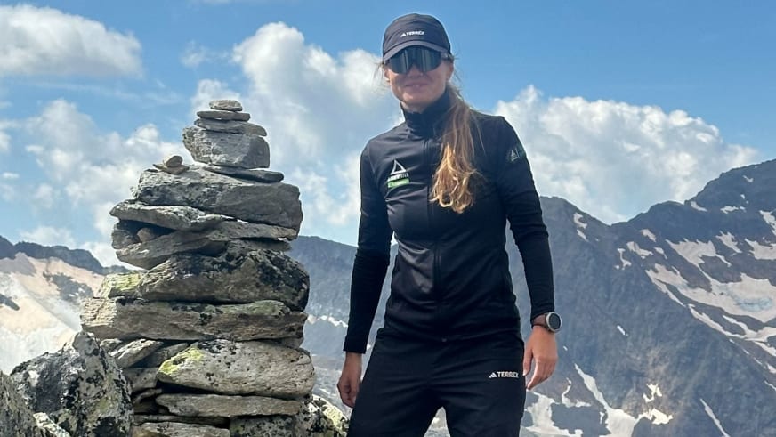 Mit schwarzer Kappe und Sonnenbrille steht Bergwanderführerin Madlen Bucher neben Steinmännchen vor Hochgebirgspanorama.