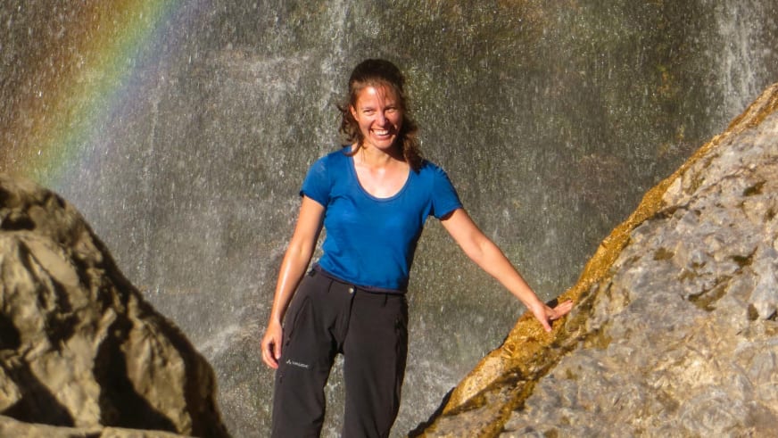 Bergwanderführerin Anna Bodenstedt lächelt in die Kamera mit braunen Haaren und blauem T-Shirt vor einer grauen Felswand.