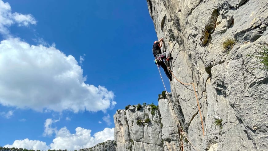 An heller Kalksteinwand klettert Jakob Fink als Bergführer aufwärts, mit Helm und orangem Kletterseil gesichert.